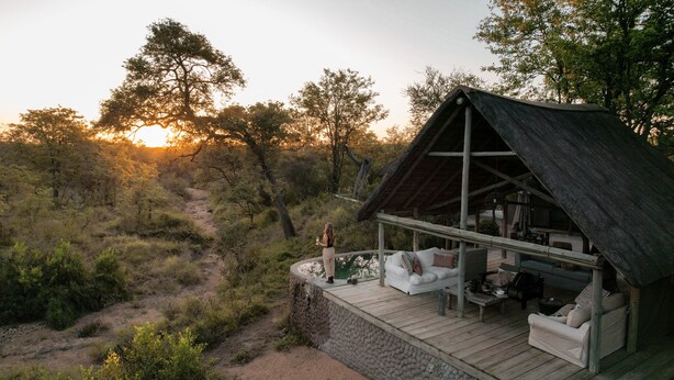 A rustic cabin with a thatched roof, a wooden deck, and a seating area with cushions. - Nsala Wilderness Camp (Hoedspruit)