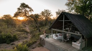 A rustic cabin with a thatched roof, a wooden deck, and a seating area with cushions. - Nsala Wilderness Camp (Hoedspruit)