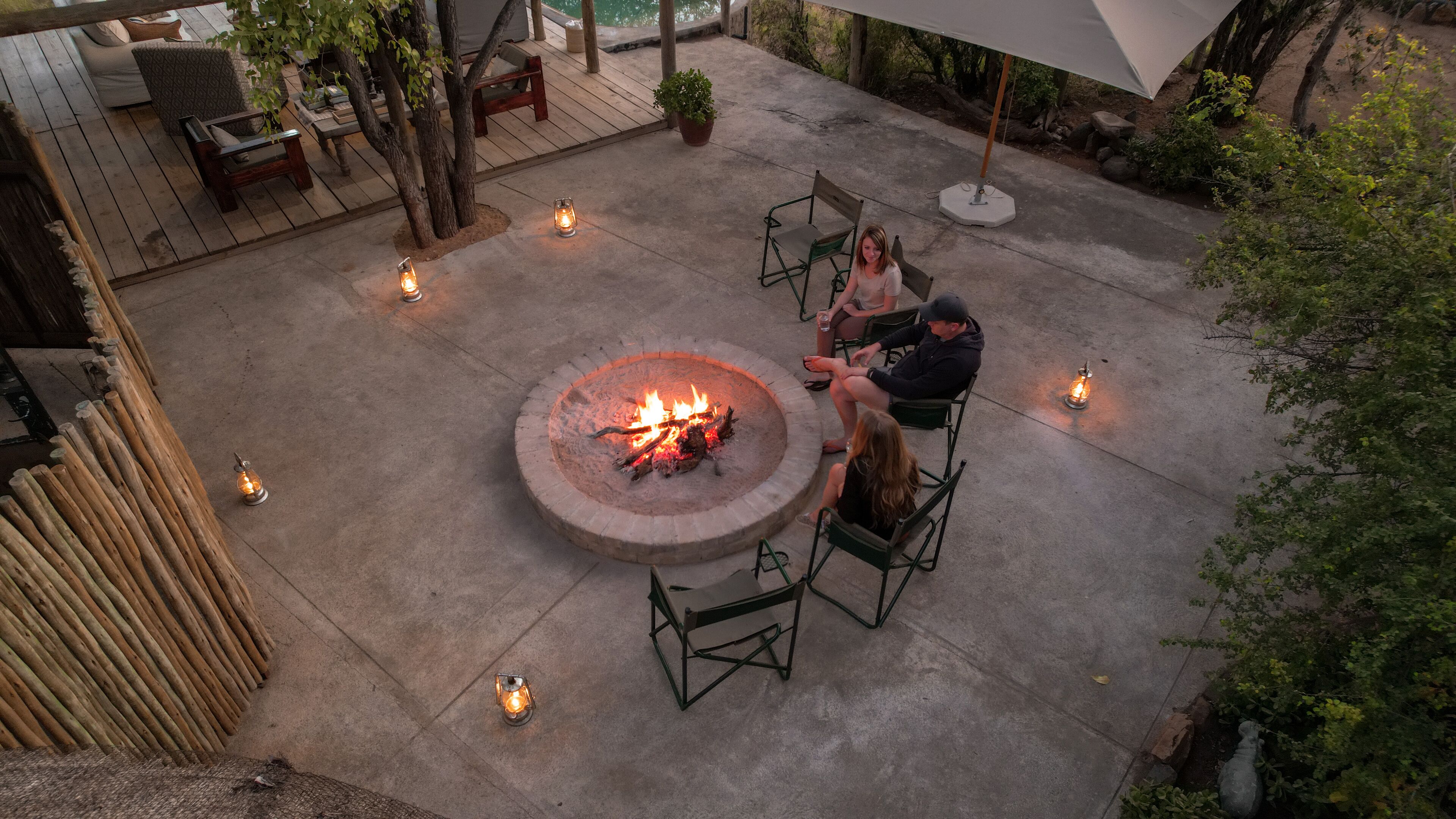 An outdoor patio area with a central fire pit, seating arrangements, and surrounding lanterns.