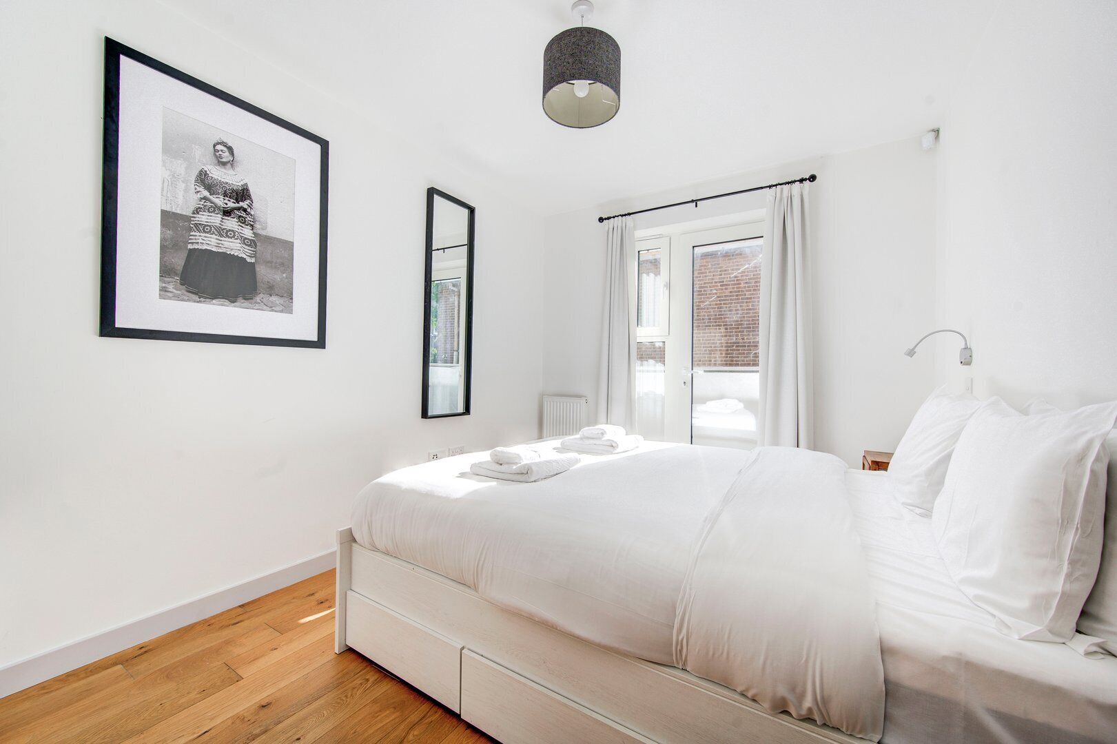 A modern bedroom with a large bed, a framed picture on the wall, and a window with curtains.