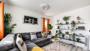 A modern living room with a grey sofa, a small round table, and a bookshelf filled with plants and decorative items. - GuestReady - Urban Comfort near Wembley Stadium (London)