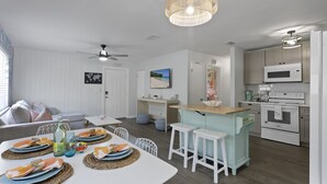 Une cuisine moderne avec des appareils électroménagers blancs, un coin repas avec une table blanche dressée pour quatre personnes, et un ventilateur de plafond.