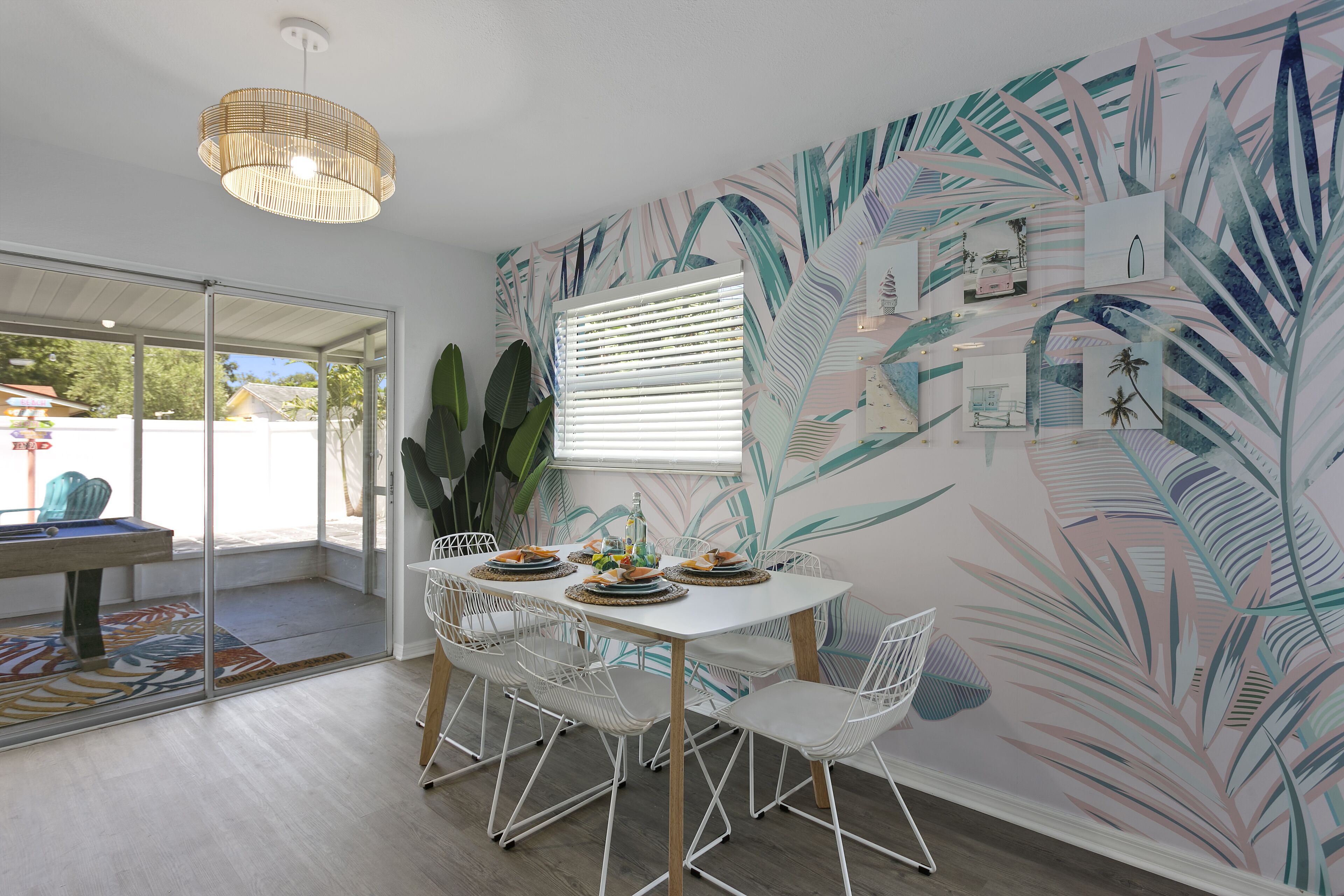 A dining area with a white table, white chairs, and a tropical leaf-patterned wall.