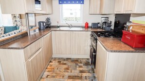 Une cuisine compacte avec des meubles en bois, un plancher à motifs en chevrons, un évier, une cuisinière et un grille-pain.