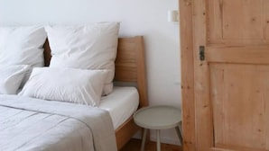 Un dormitorio con una cama, almohadas, una mesita redonda y una puerta de madera.