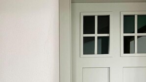 Puerta blanca con manija de latón y cerradura, con un pequeño ventanal encima de la manija.