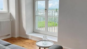 Una sala de estar moderna con un sofá gris, una mesita redonda y un amplio ventanal con vistas a un balcón.