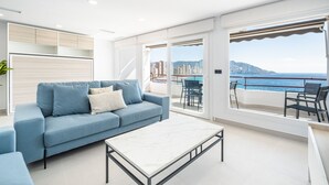 A modern living room with a blue sofa, a white coffee table, and a city view through large windows. - Lux Center 5-C Deluxe Beach Apartment-Old Town (Benidorm)