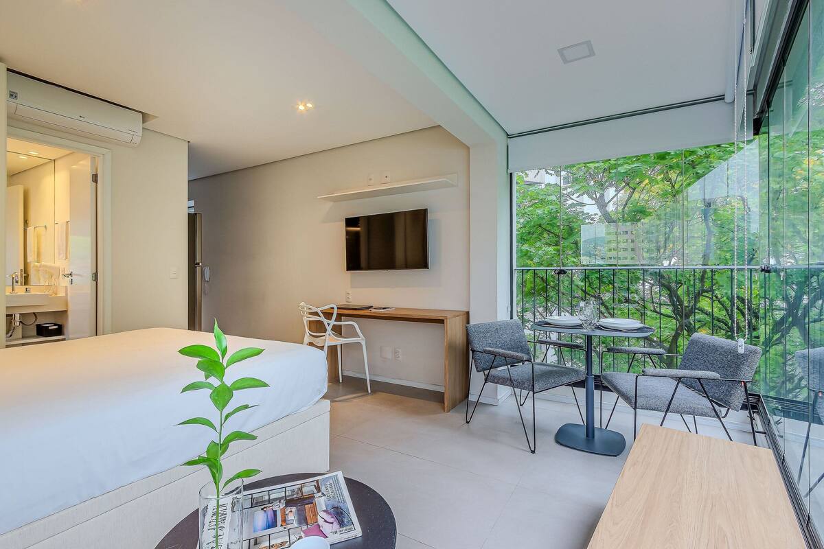 A modern hotel room with a bed, desk, and balcony with a view.
