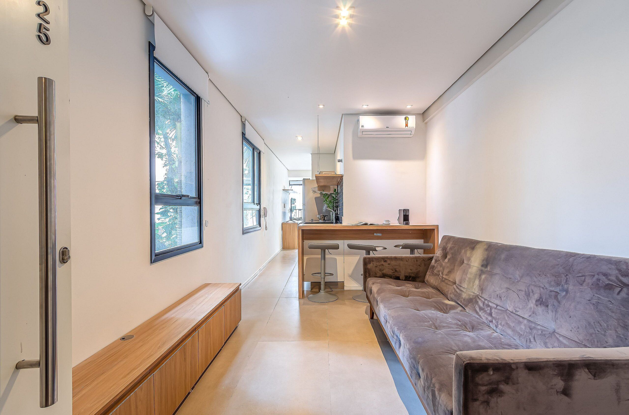 A modern interior with a sofa, a wooden bench, a kitchen area, and a large window.