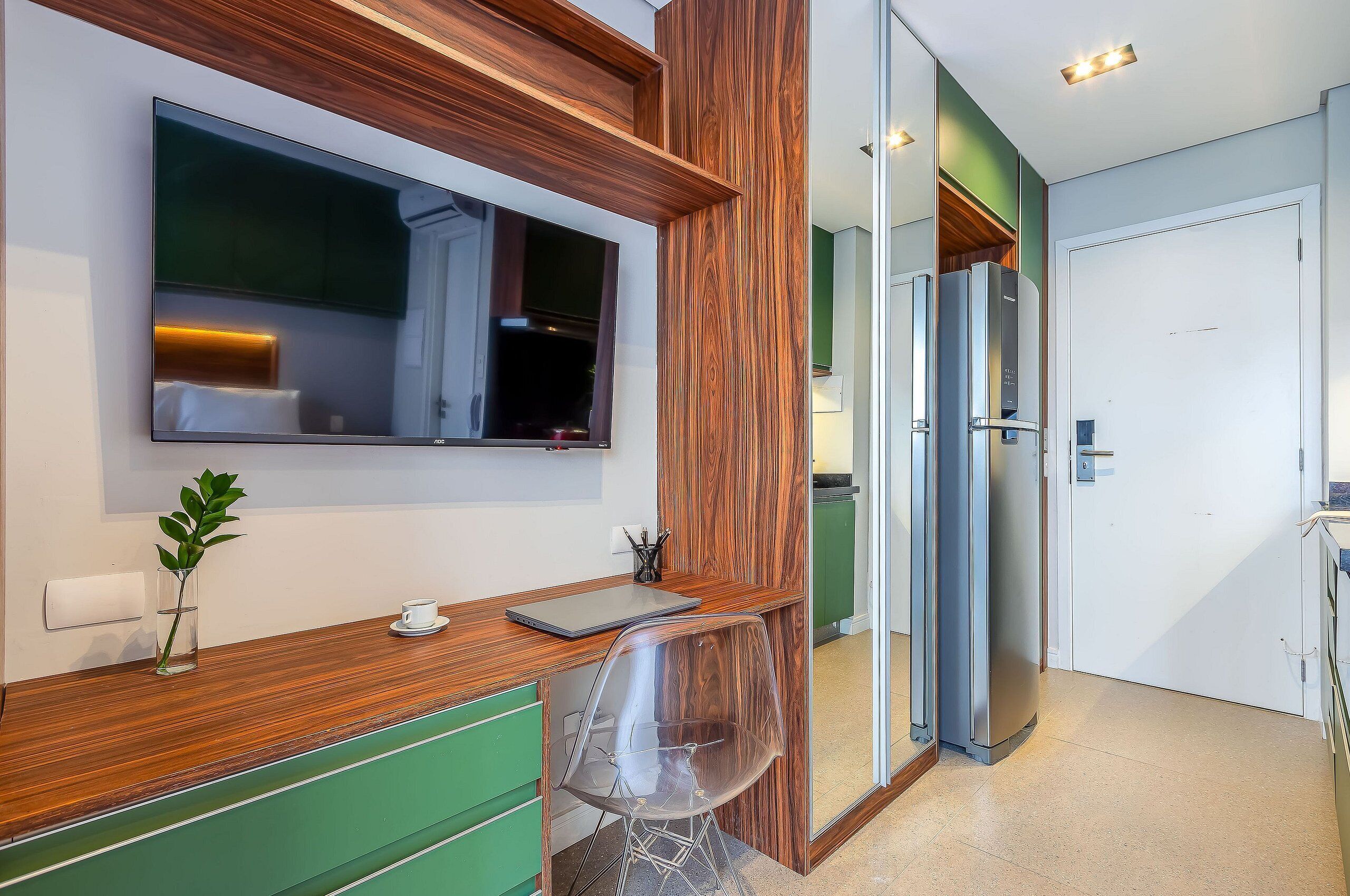 A modern kitchen with a built-in TV, wooden accents, a green cabinet, and a clear chair.