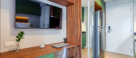 A modern kitchen with a built-in TV, wooden accents, a green cabinet, and a clear chair.