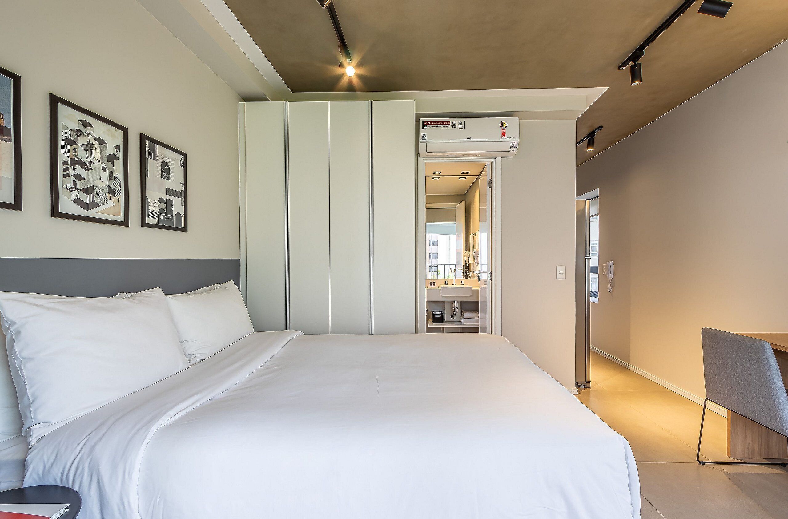 Una habitación de hotel moderna con una cama grande, un escritorio, una silla y un baño visible a través de una puerta abierta.