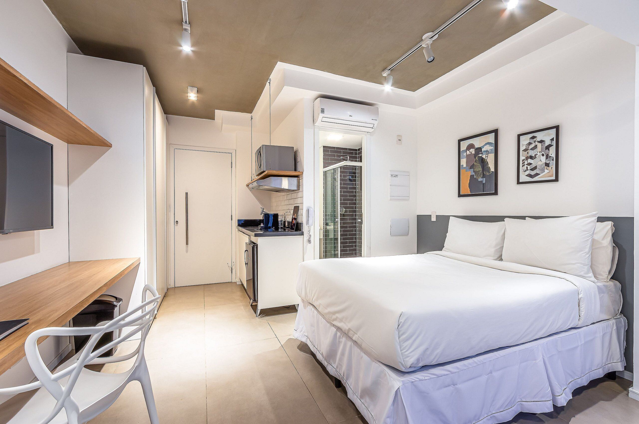 Una habitación compacta con cama, escritorio y silla. Incluye una kitchenette con estufa y microondas.