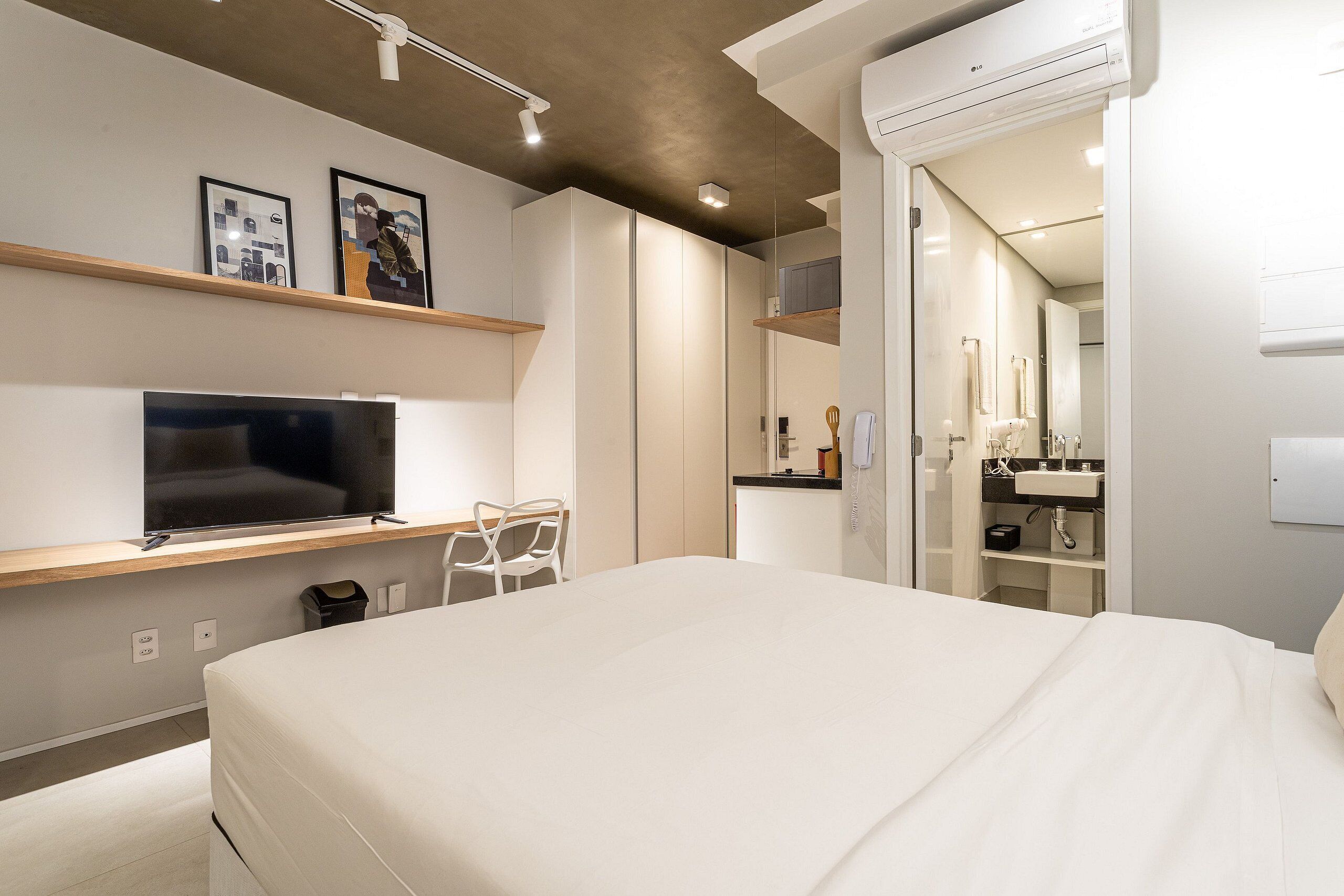 A modern hotel room with a bed, a TV, a desk, and a bathroom with a mirror and sink.