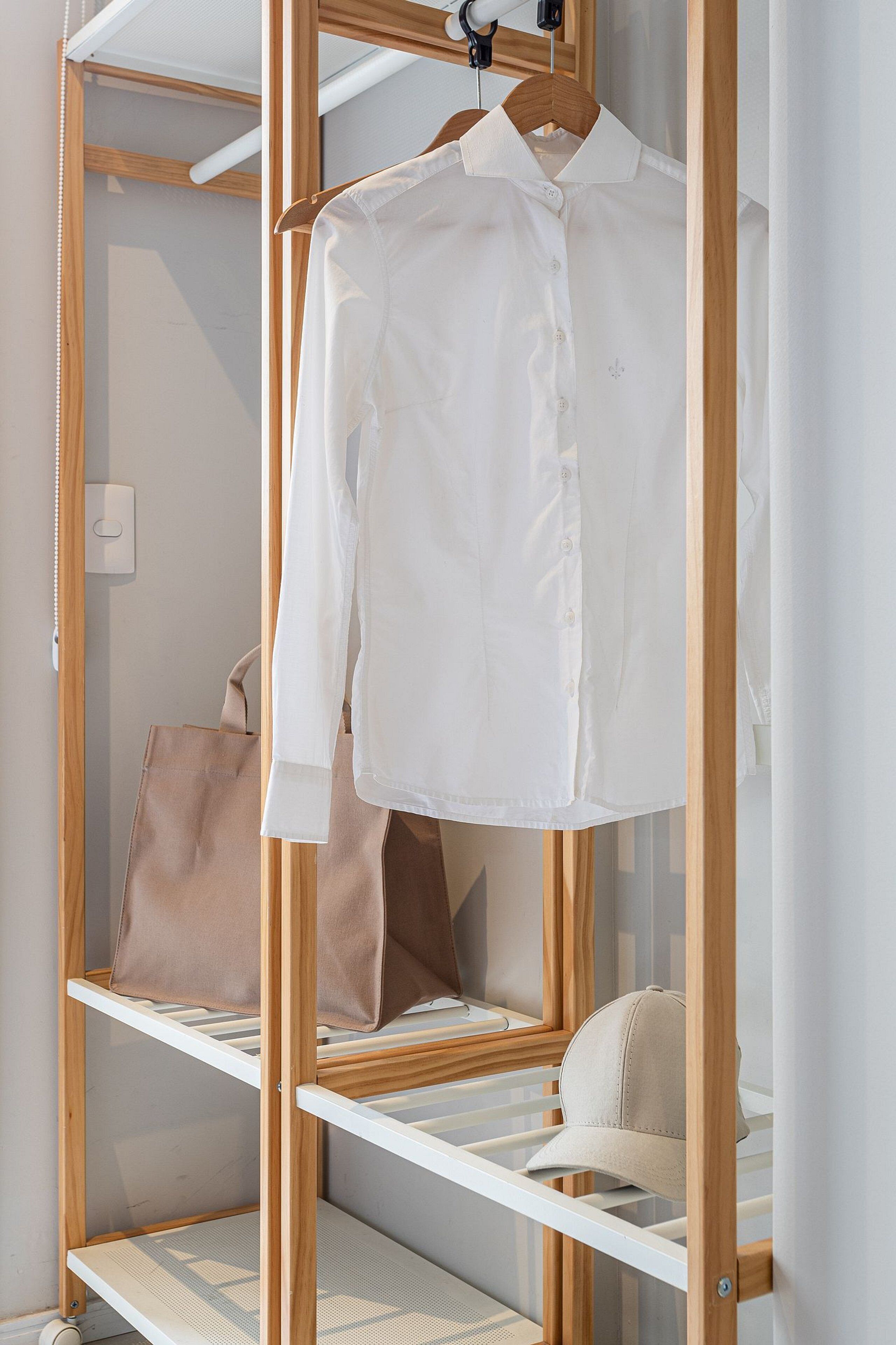 A white shirt hanging on a wooden hanger in a closet with shelves.