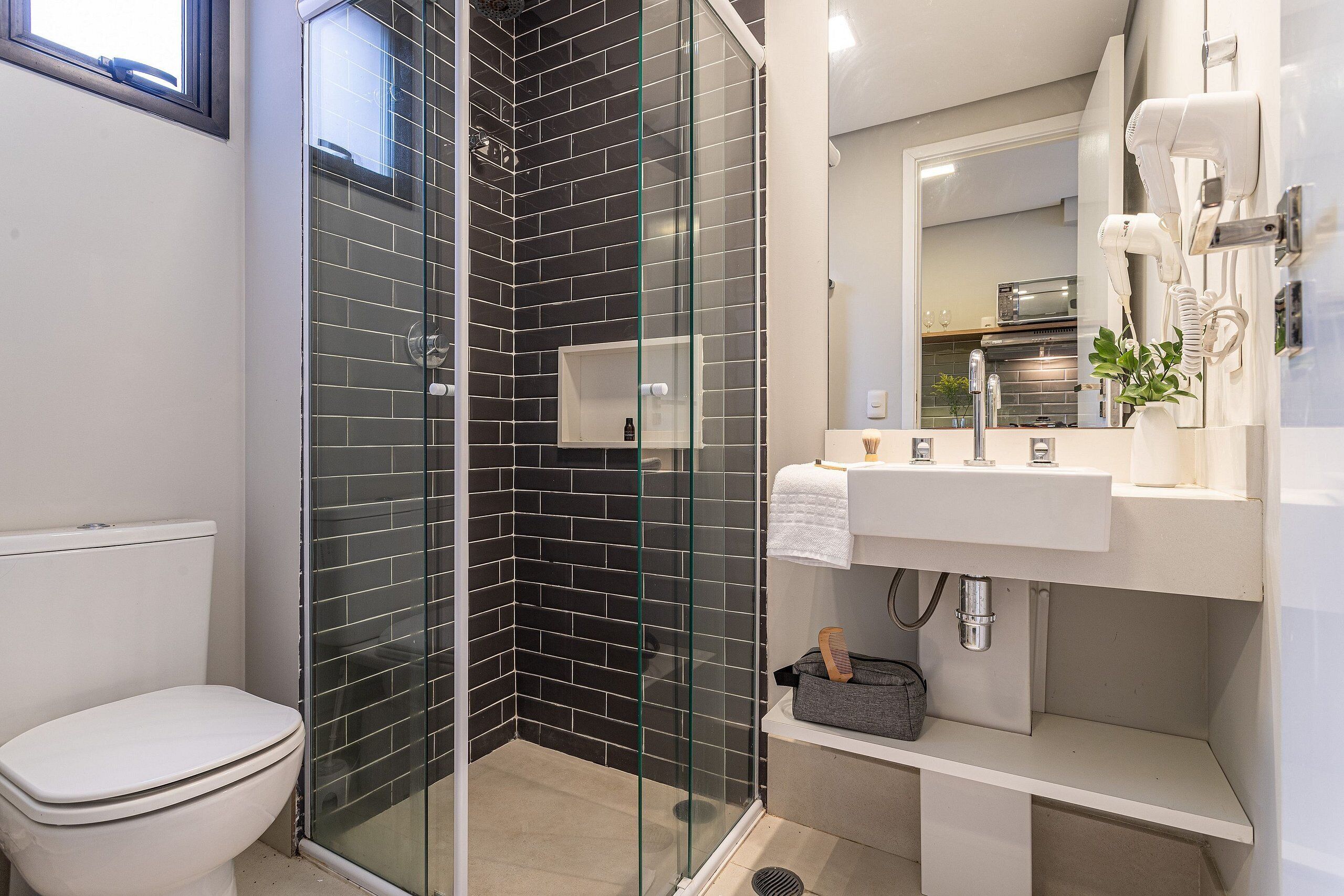 A bathroom with a glass-enclosed shower, a white toilet, a sink with a mirror, and a hairdryer mounted on the wall.