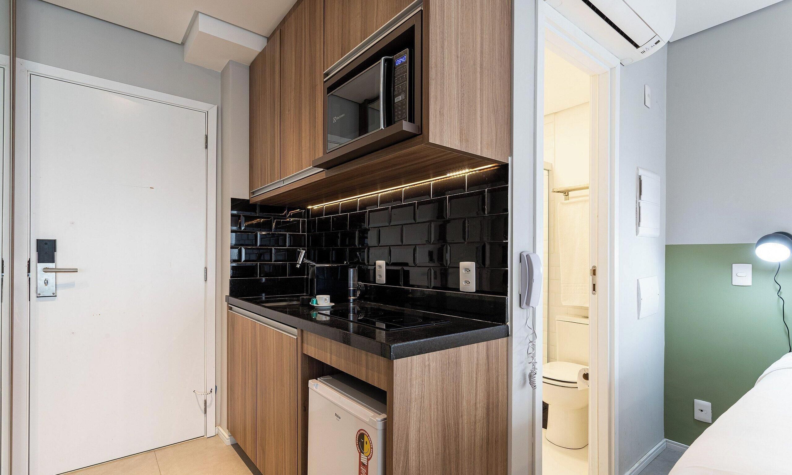 Une cuisine de taille réduite, équipée d’un four à micro-ondes, d’un plan de travail noir et de meubles en bois.