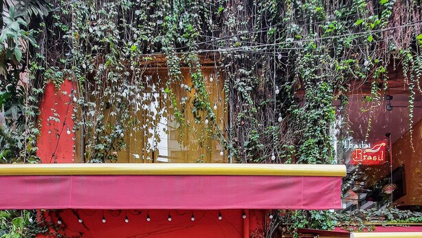 An outdoor dining area with tables and chairs, a bar with shelves of bottles, and a red wall. - Next Home Design by Viva - Apartamentos em prédio próximo ao Parque do Ibirapuera (São Paulo)