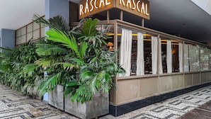 A building with a sign reading 'RASCAL RASCAL' and large potted plants in front. - Next Home Design by Viva - Apartamentos em prédio próximo ao Parque do Ibirapuera (São Paulo)