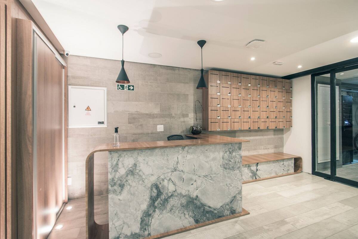 A reception area with a marble counter, wooden cabinets, pendant lighting, and a glass door leading to another room.