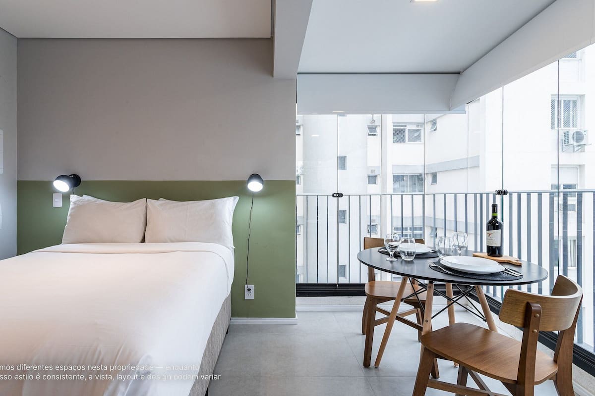 A hotel room with a bed, a dining table with chairs, and a balcony with a railing.