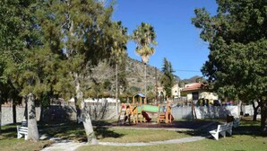 A park with playground equipment, a stone pathway, and a house in the background. - Beautiful 3 Bedr House in Arakapas With Fireplace (Arakapas)