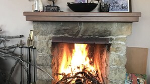 A stone fireplace with a fire, a shelf above with various items, and a bicycle to the left. - Beautiful 3 Bedr House in Arakapas With Fireplace (Arakapas)