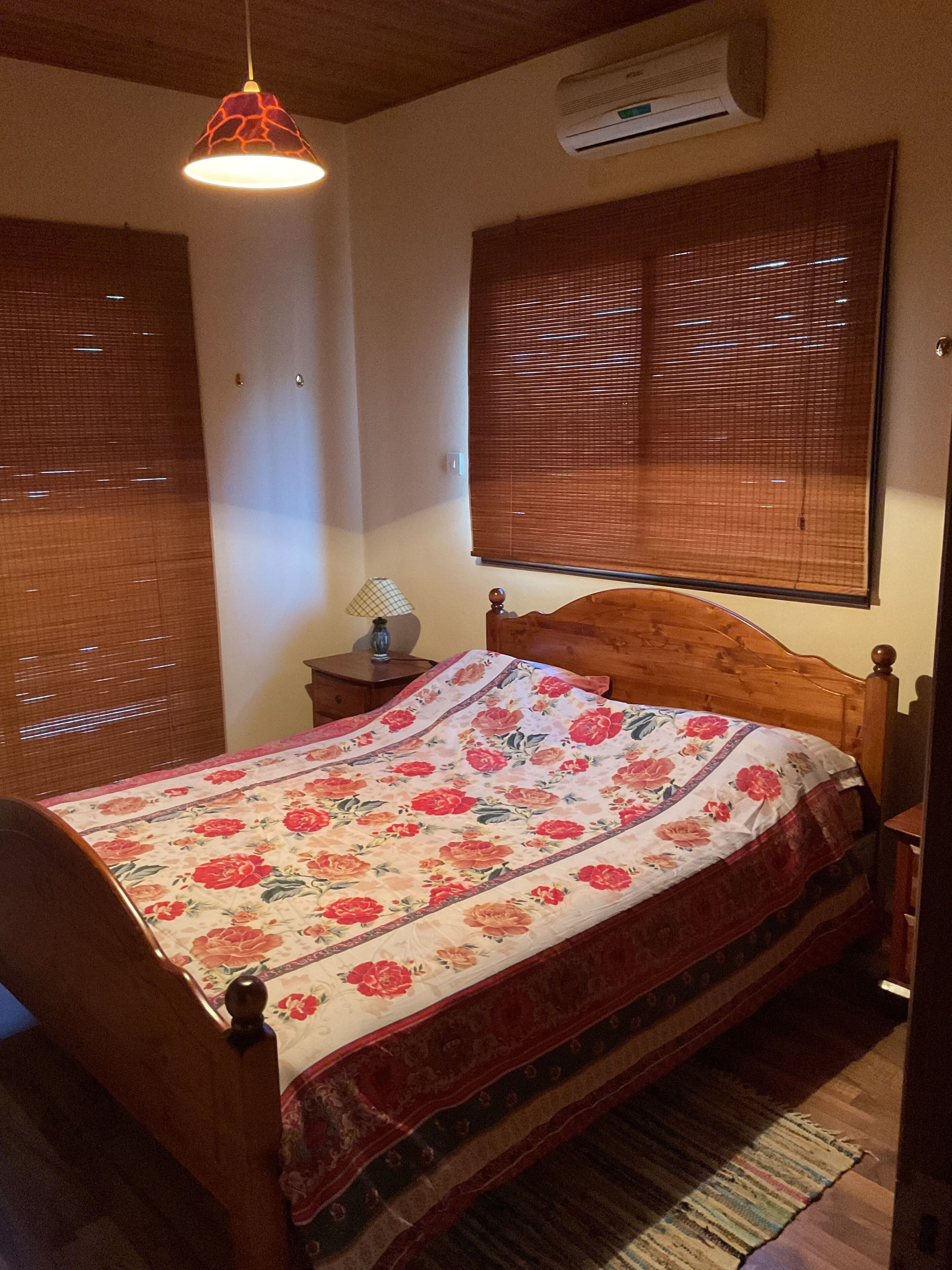 Un dormitorio con una cama de madera, una lámpara colgante, una mesita de noche y una ventana con persianas.