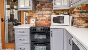 Une cuisine avec un mur en briques, des meubles blancs, un four à micro-ondes et une cuisinière.