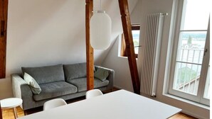 En moderne stue med et hvidt bord og stole, en grå sofa og et stort vindue med udsigt.