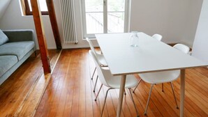 Et værelse med trægulv, et hvidt bord og stole, en grå sofa og et vindue med persienner.
