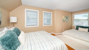 Un dormitorio con dos camas, una ventana con persianas, una lámpara y un cuadro en la pared.