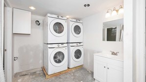 Un lavadero con cuatro lavadoras apiladas, un armario blanco, un lavabo con espejo y luces empotradas en el techo.