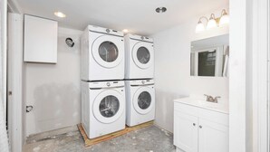 A laundry room with four stacked washing machines, a white cabinet, a sink with a mirror, and recessed ceiling lights.