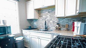 Une cuisine moderne avec des meubles blancs, une cuisinière à gaz, un évier et un four à micro-ondes.