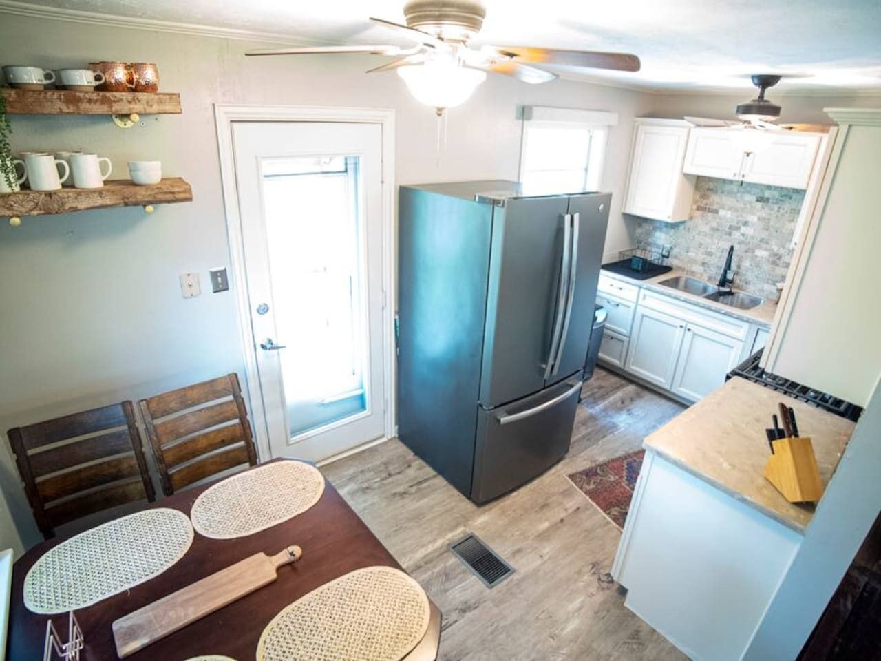 Una cocina compacta con refrigerador, una mesa de comedor con individuales y un ventilador de techo.
