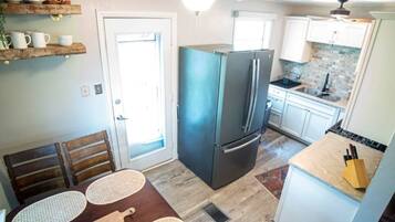 Una cocina compacta con refrigerador, una mesa de comedor con individuales y un ventilador de techo.