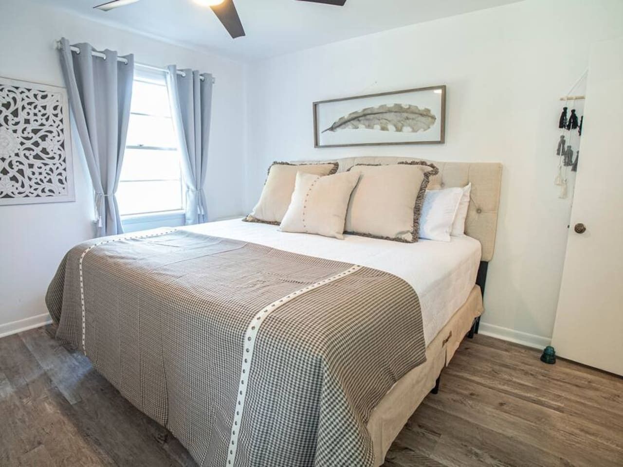 Un dormitorio con cama, cortinas, una obra de arte en la pared y una puerta.