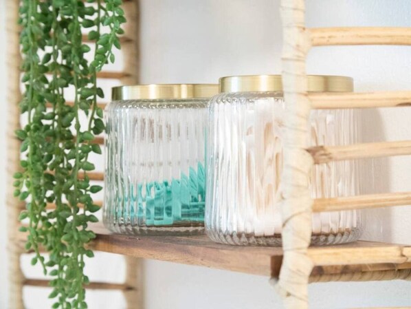 A shelf with glass jars containing white objects, possibly cotton swabs, and a green plant hanging beside it.