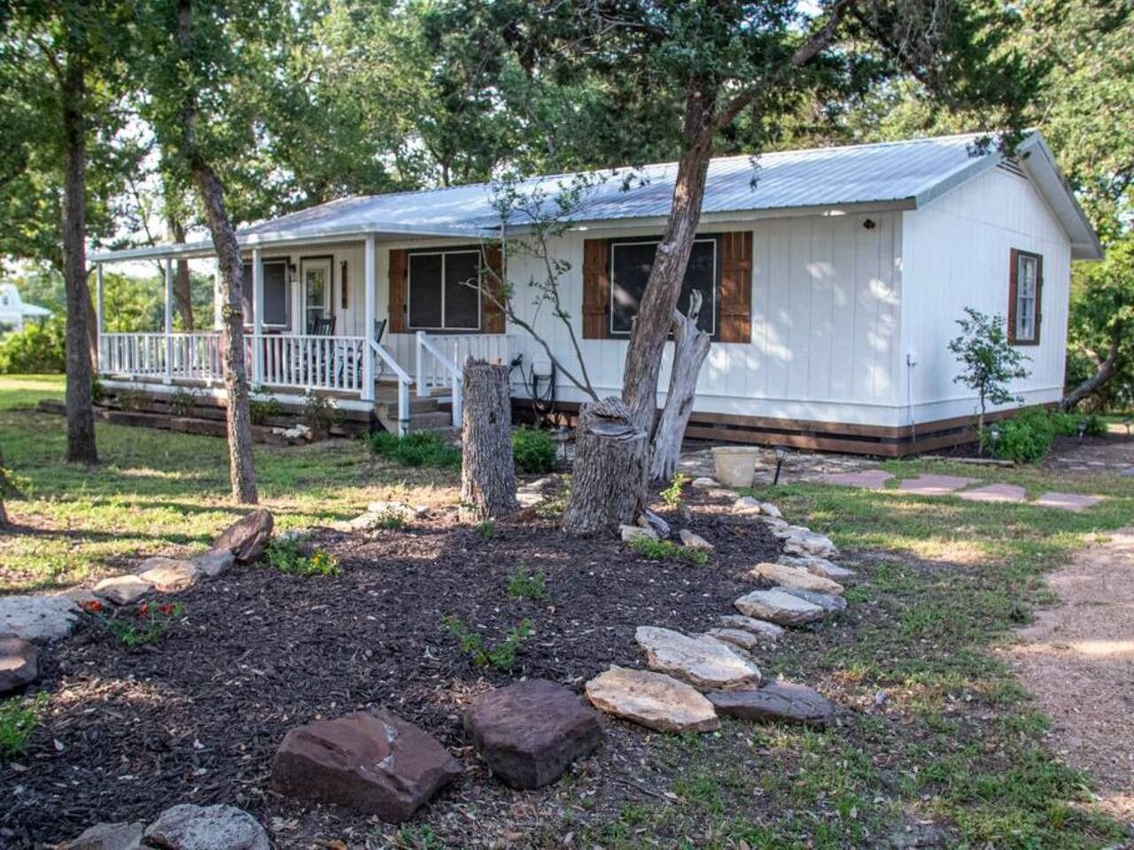 Casa móvel térrea com varanda, cercada por um jardim ajardinado com pedras e árvores.