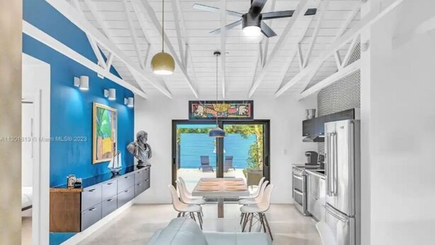 A modern kitchen with stainless steel appliances, a dining area with a light blue sofa, and a ceiling fan.