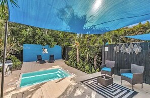 Uma área de piscina com toldo azul, espreguiçadeiras e deck de madeira.