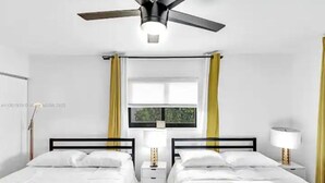 A hotel room with two beds, a ceiling fan, a window with curtains, and a bedside lamp.