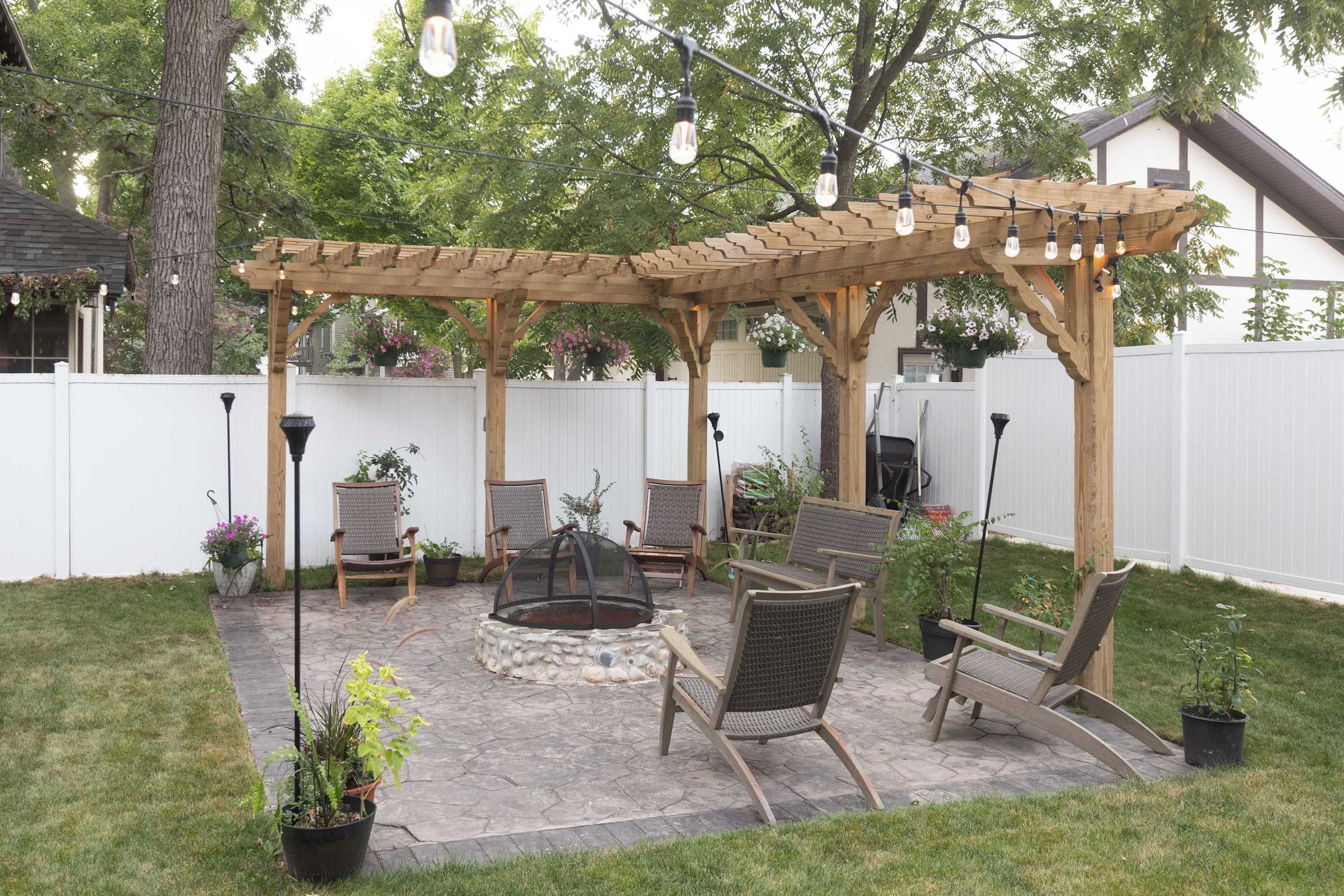 Un patio aménagé dans le jardin, avec une pergola, des sièges d’extérieur et un foyer.
