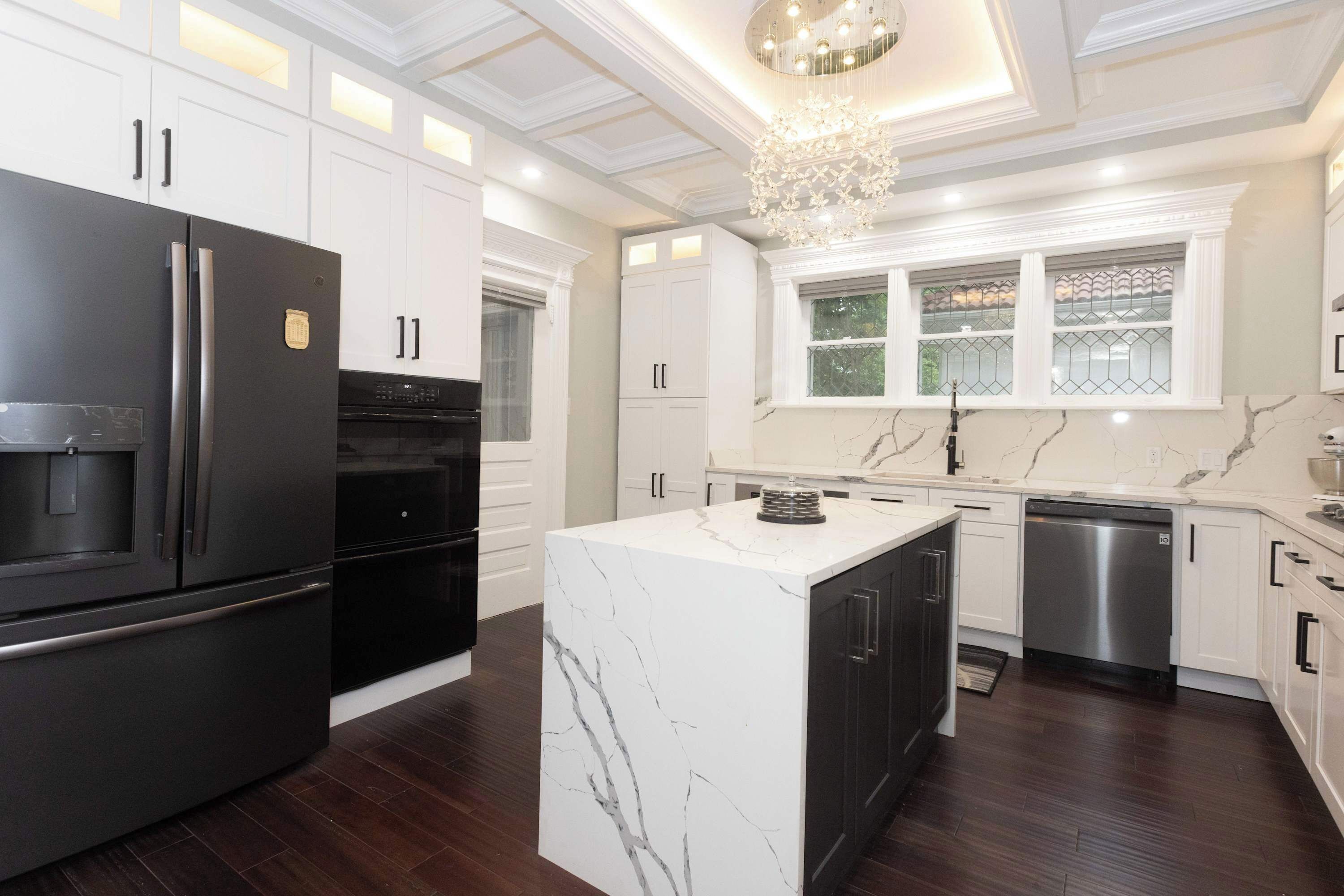 A modern kitchen with white cabinetry, a marble island, and stainless steel appliances.