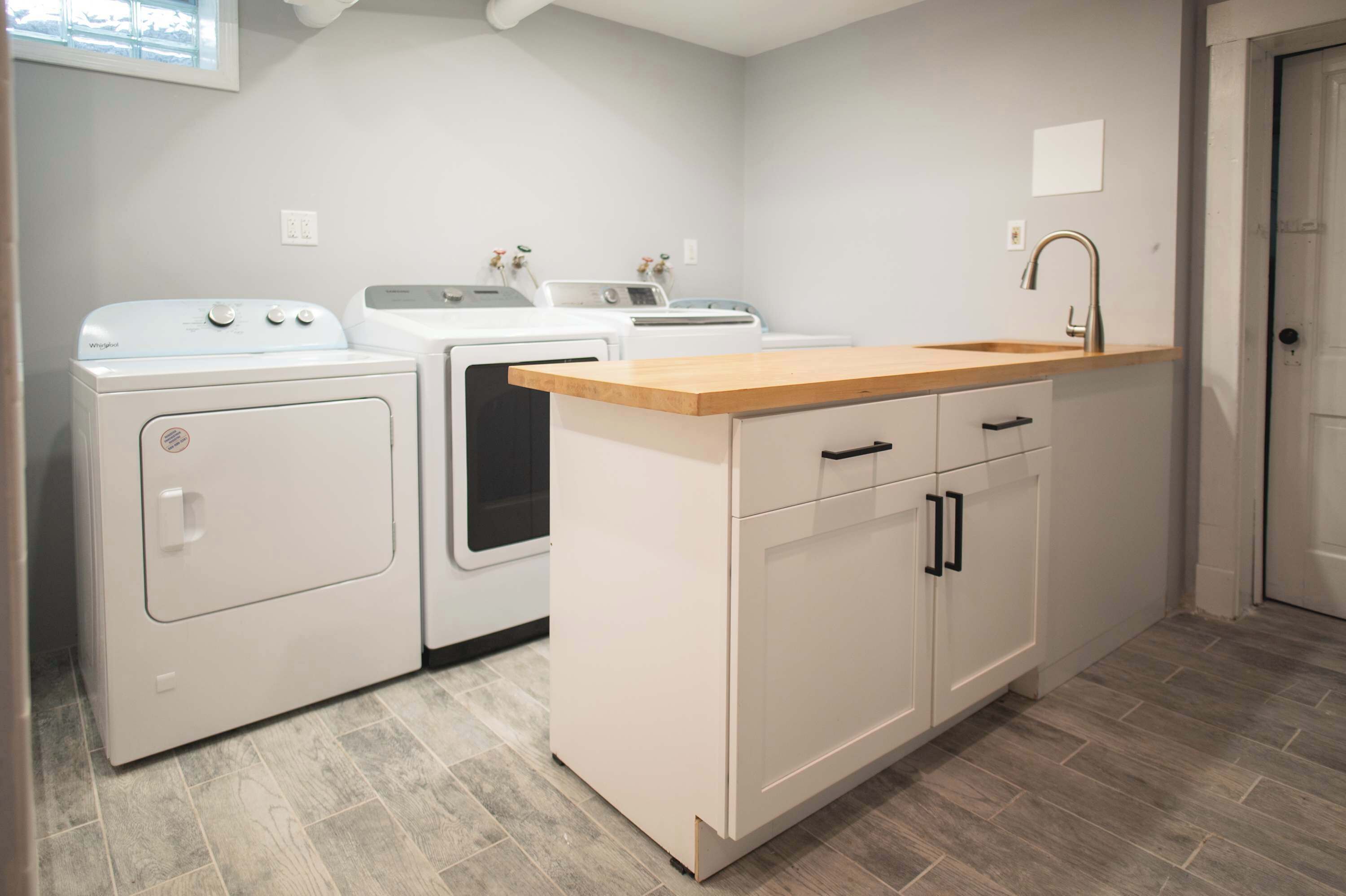 A laundry area with a washing machine, dryer, and a sink with wooden countertop.