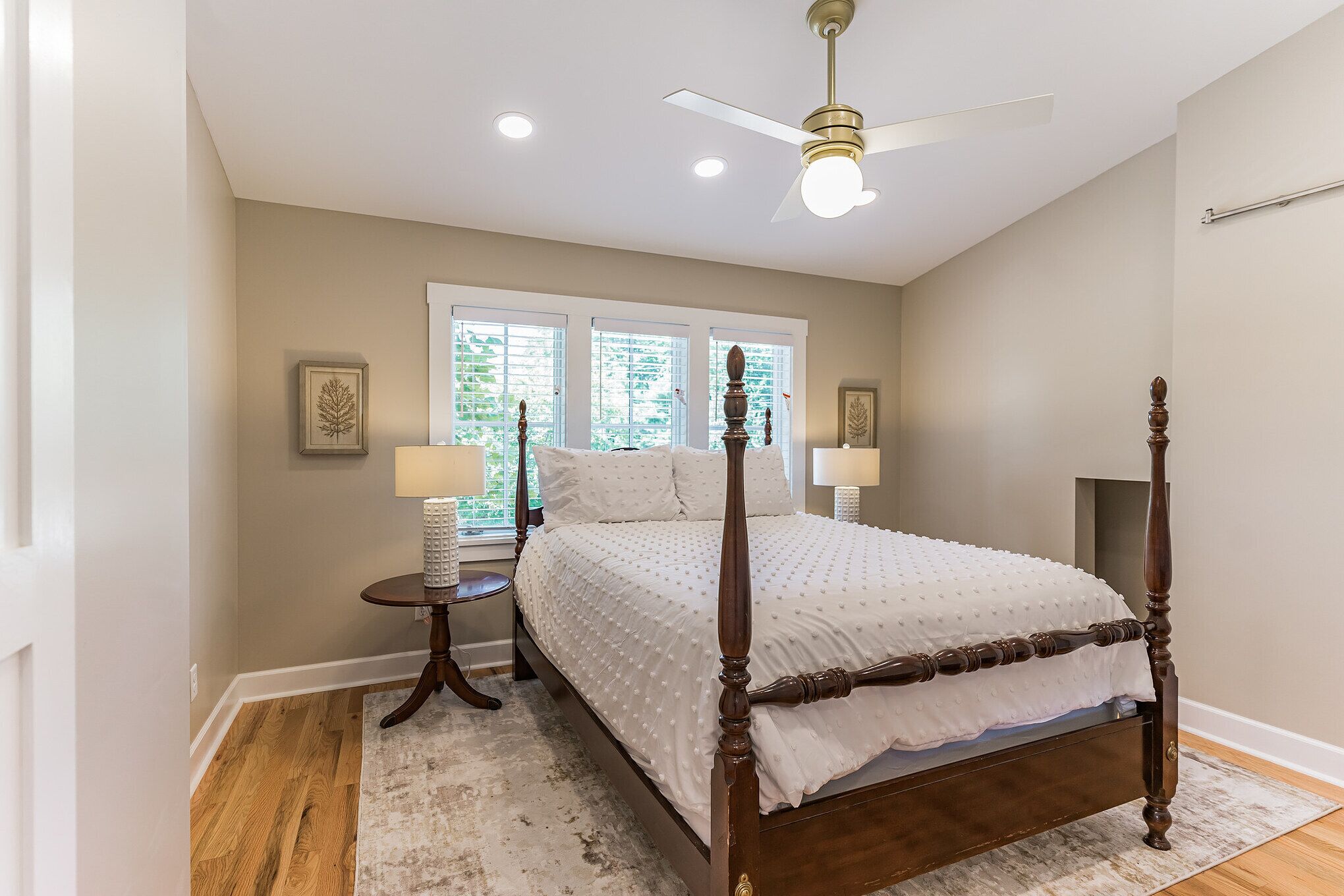A bedroom with a four-poster bed, a ceiling fan, and two bedside lamps.