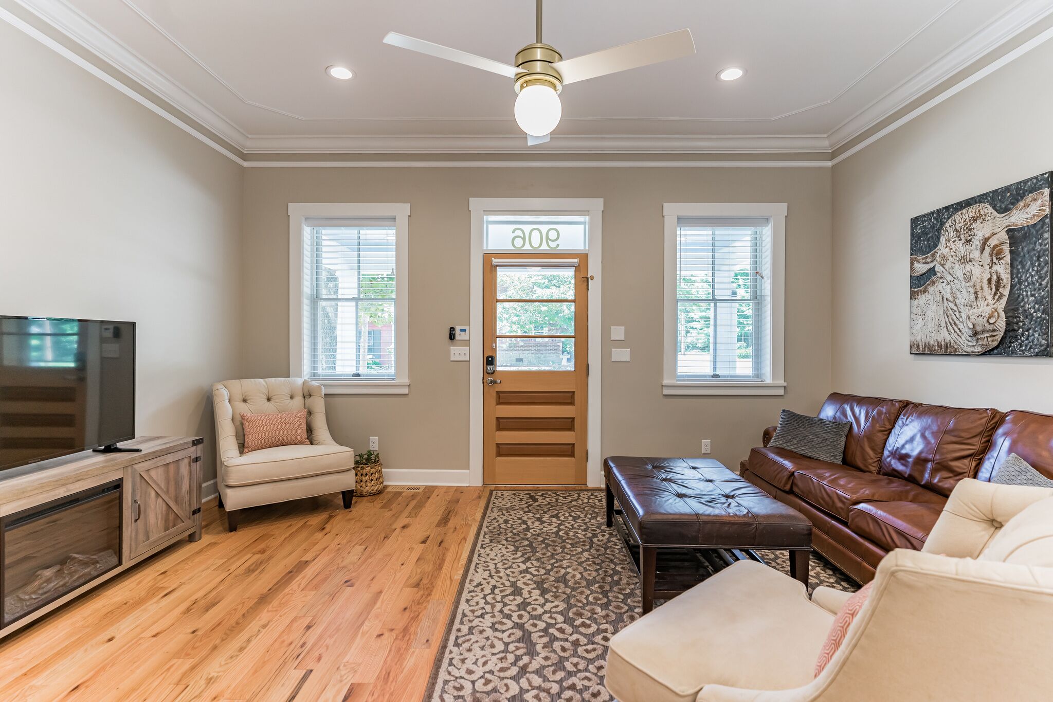 A living room with a wooden floor, a beige sofa, a brown leather couch, a TV, and a ceiling fan.