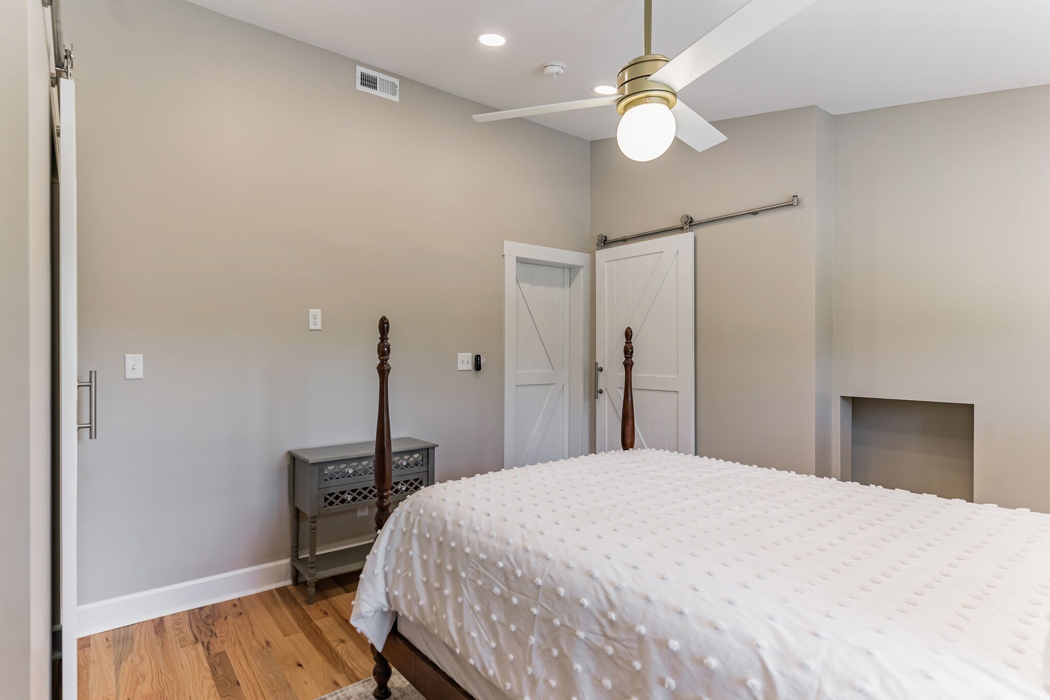 A bedroom with a bed, a nightstand, a wardrobe, a ceiling fan, and a fireplace.